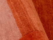Nahaufnahme eines Wollteppichs in verschiedenen Rottönen, von der Seite betrachtet.