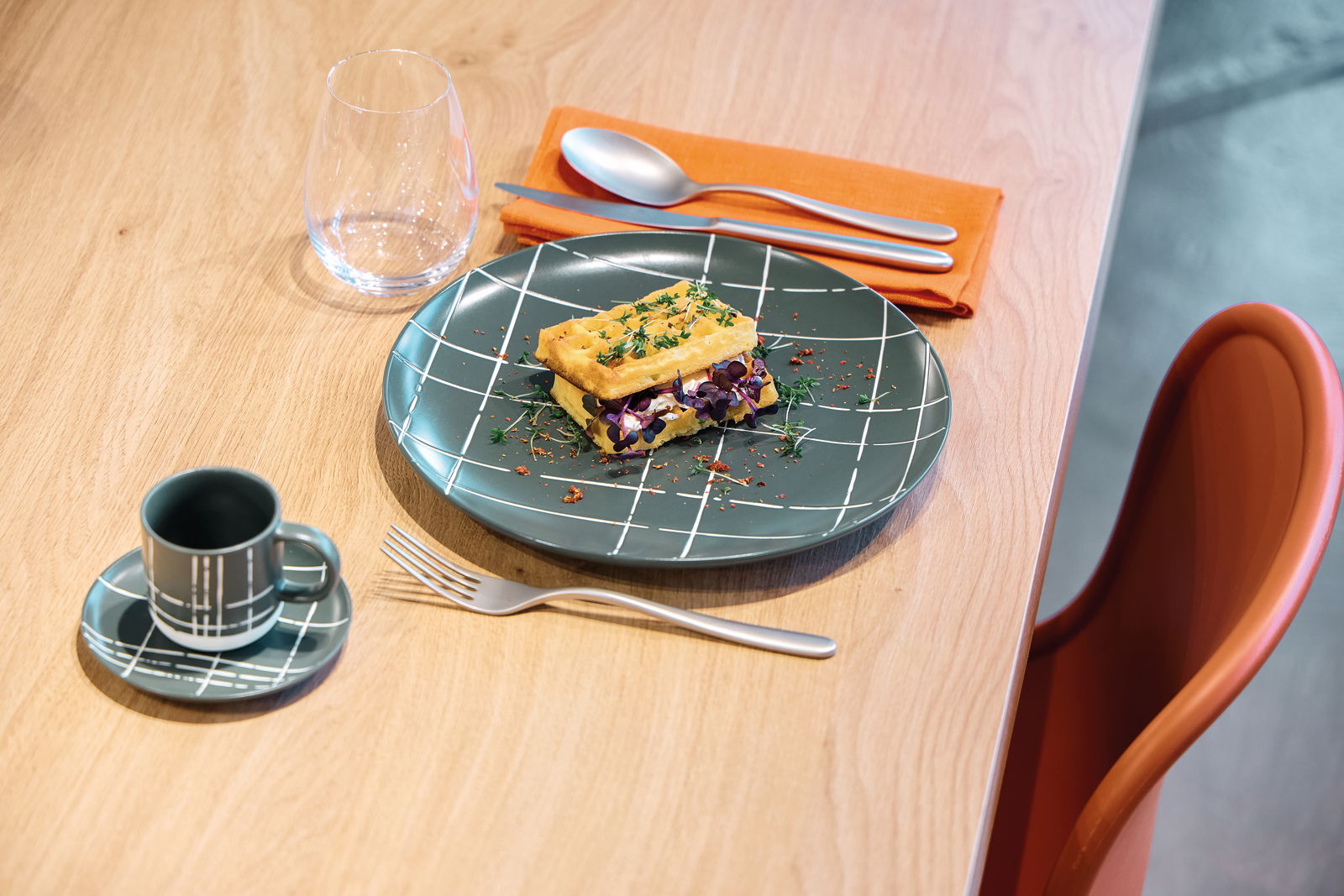 Tiefer Teller mit modernem Karomuster, serviert mit einer Waffel und Kräutern, aus der Vogelperspektive auf einem Holztisch.