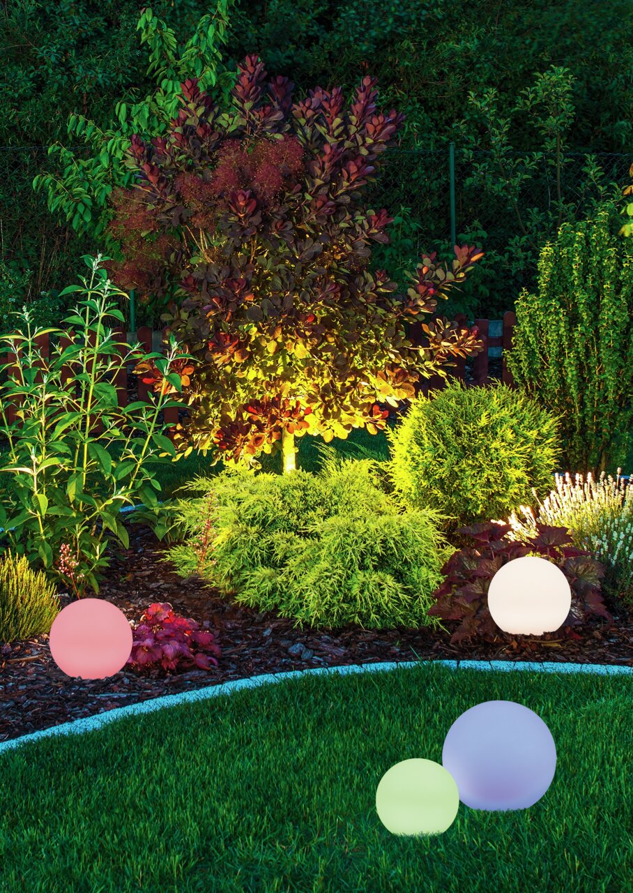 Reality Leuchten Solar- Außenleuchte MELO Verschiedene farbige Solar-Außenleuchten in Kugelform, die in einem Garten bei Nacht leuchten. Perspektive: seitlich auf die Leuchten und den Garten gerichtet.