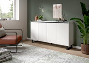 Modernes weißes Sideboard mit vier Türen, schwarzem Sockel und dekorativen Elementen, seitliche Perspektive.