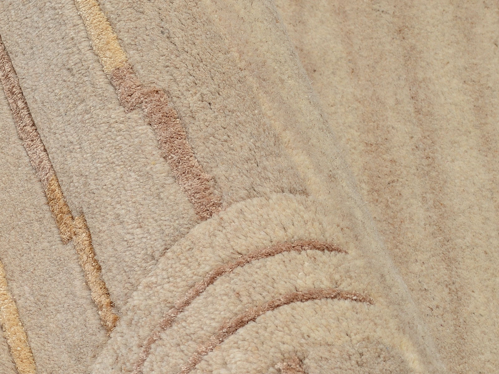 Nahaufnahme eines beigen Wollteppichs mit dezenten Streifen in verschiedenen Brauntönen, perspektivisch von der Seite aufgenommen.