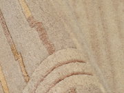 Nahaufnahme eines beigen Wollteppichs mit dezenten Streifen in verschiedenen Brauntönen, perspektivisch von der Seite aufgenommen.