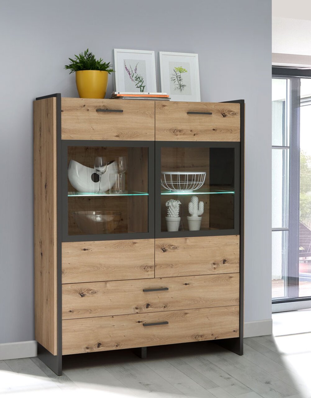 Moderne Highboardvitrine aus Holz mit Glastüren, dekoriert mit Pflanzen und Geschirr, seitliche Perspektive