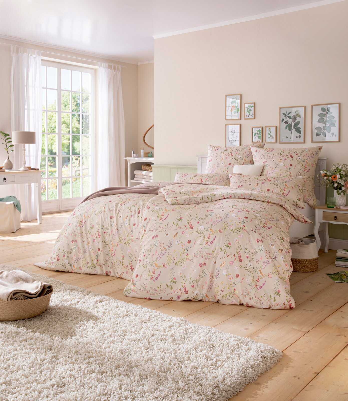 Gemütliches Schlafzimmer mit floraler Bettwäsche in Pastelltönen, Tageslicht durch großes Fenster, seitliche Perspektive