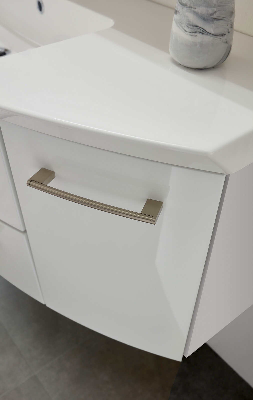 Nahaufnahme eines weißen Badezimmerschranks mit modernem Griff, von oben betrachtet.