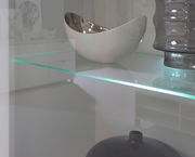 Nahaufnahme einer Vitrine mit Glasregal, auf dem eine silberne Schale und eine graue Vase stehen.