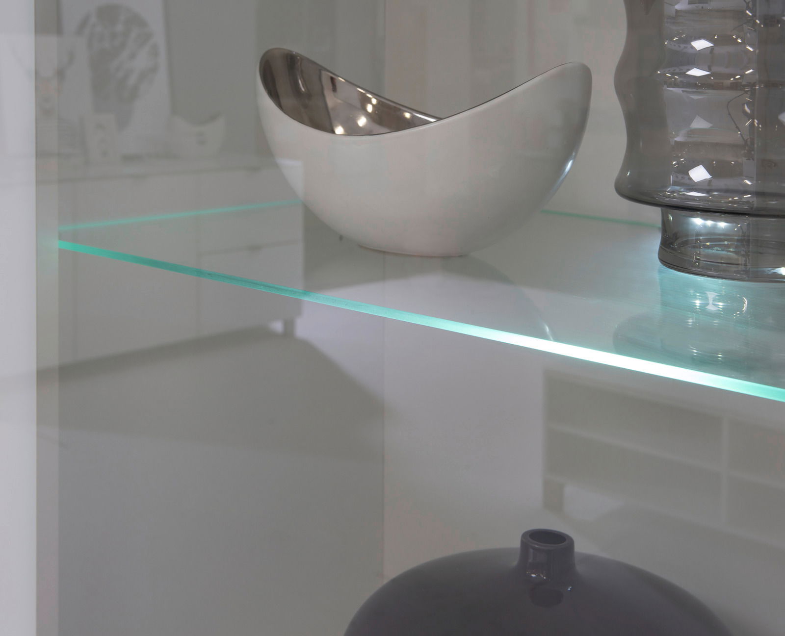 Nahaufnahme einer Vitrine mit Glasregal, auf dem eine silberne Schale und eine graue Vase stehen.