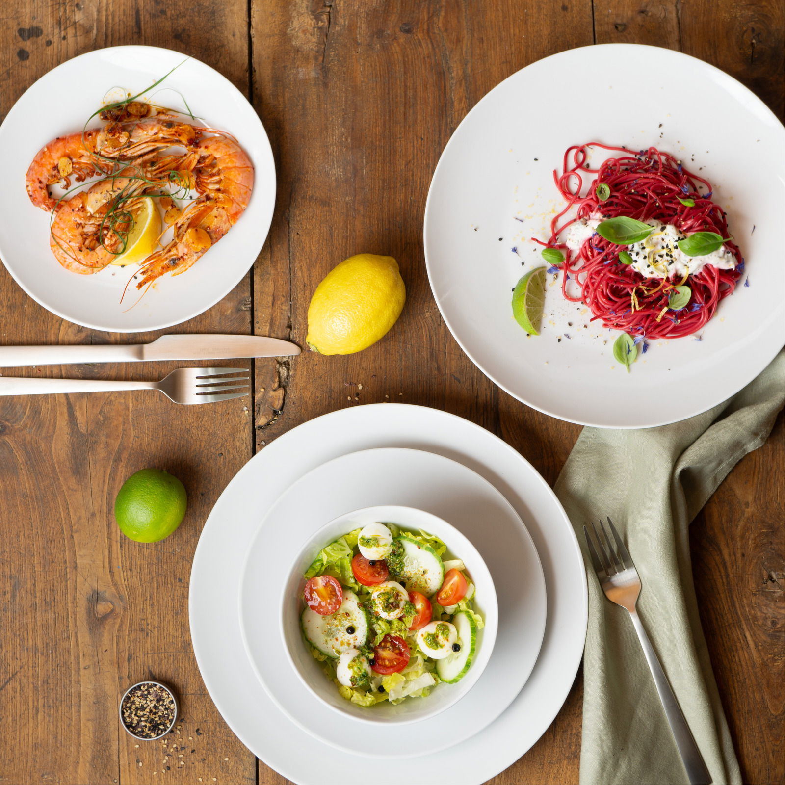 Moritz & Moritz Geschirrset 18-tlg. BASIC Vogelperspektive auf ein Geschirrset mit drei Tellern, die mit Garnelen, Salat und Pasta angerichtet sind, auf einem Holztisch.