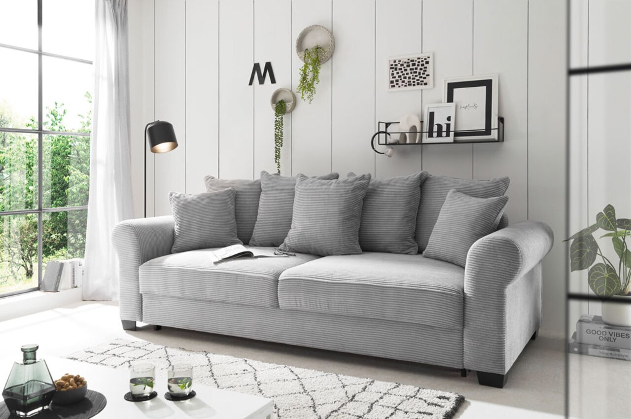 Graues Funktionssofa mit mehreren Kissen in einem modernen Wohnzimmer, seitliche Perspektive.