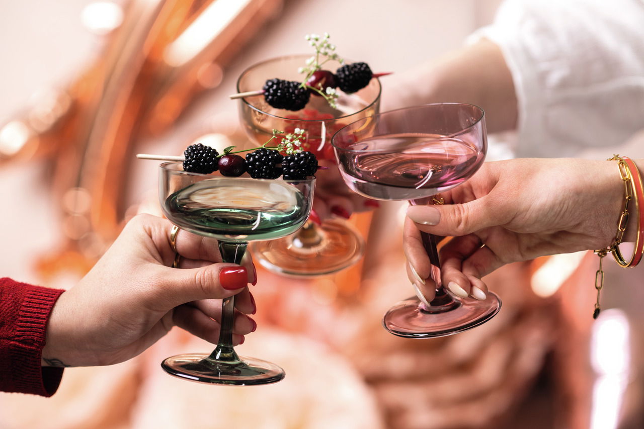 Drei elegante Sekt- und Dessertschalen in verschiedenen Farben, gefüllt mit Beeren und dekoriert mit Blumen, aus der Perspektive von oben betrachtet.