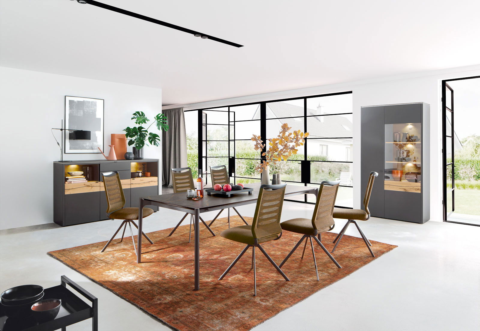 Venjakob Esstisch ET236 MIO PLUS Moderner Essbereich mit Esstisch und Stühlen auf einem roten Teppich, umgeben von großen Fenstern mit Blick ins Grüne, aus einer seitlichen Perspektive fotografiert.