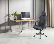 Moderner Gaming-Stuhl in Grau, seitliche Perspektive, neben einem Schreibtisch mit Computer.