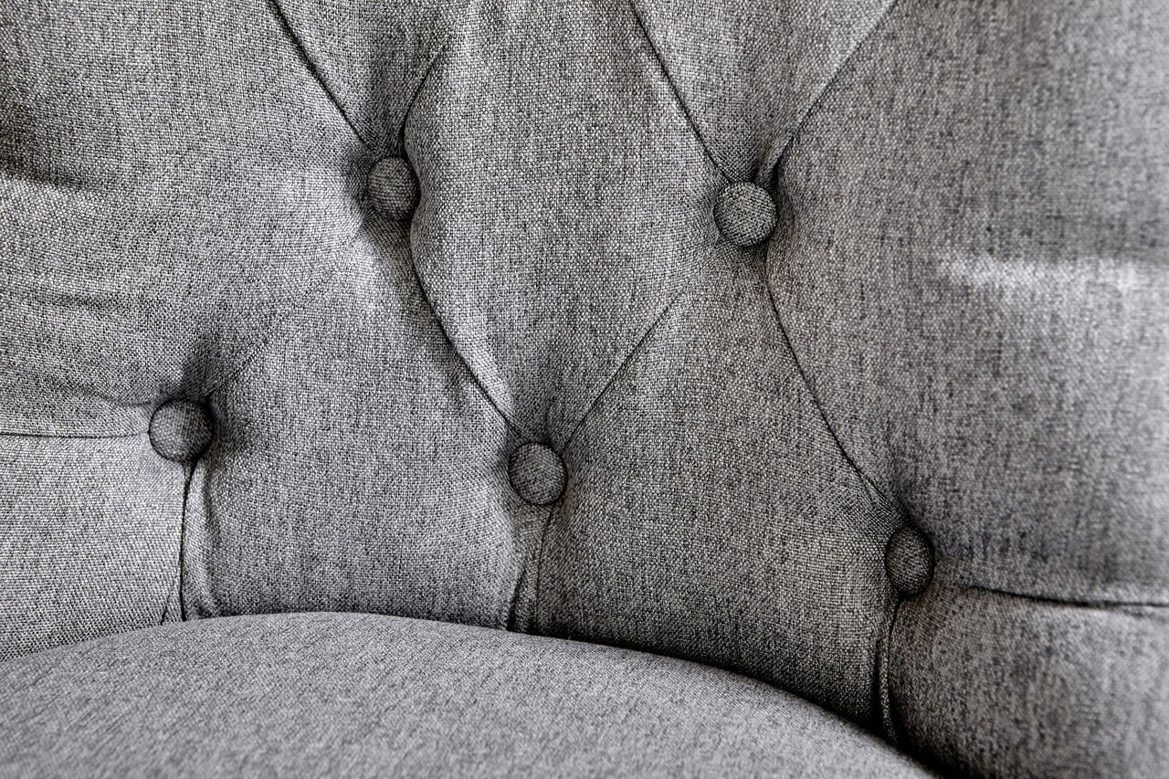 Nahaufnahme eines grauen, gepolsterten Stuhls mit Knopfdetails auf der Rückenlehne.