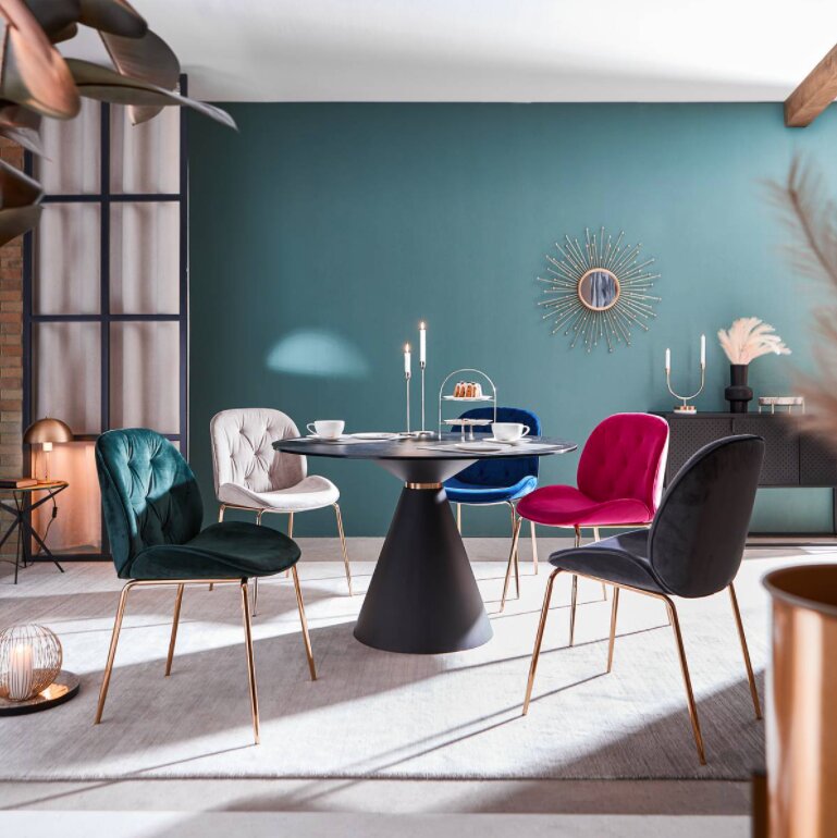 Esszimmer mit fünf eleganten Stühlen in verschiedenen Farben um einen runden Tisch, seitliche Perspektive