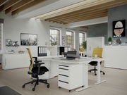 Moderne Büroumgebung mit höhenverstellbarem Schreibtisch und Rollcontainer, seitliche Perspektive