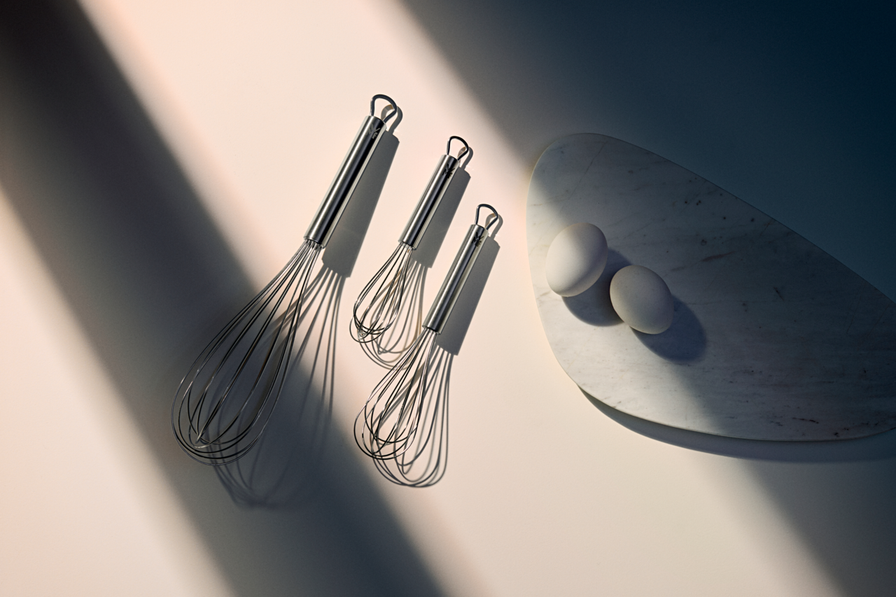 WMF Schneebesen 3-tlg. PROFI PLUS Drei Schneebesen aus Edelstahl in verschiedenen Größen, von oben betrachtet, neben zwei Eiern auf einem Marmorbrett.