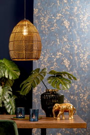 Schuin vooraanzicht van een sfeervolle goudkleurige gevlochten hanglamp boven een houten tafel met decoratieve accessoires en groene planten.