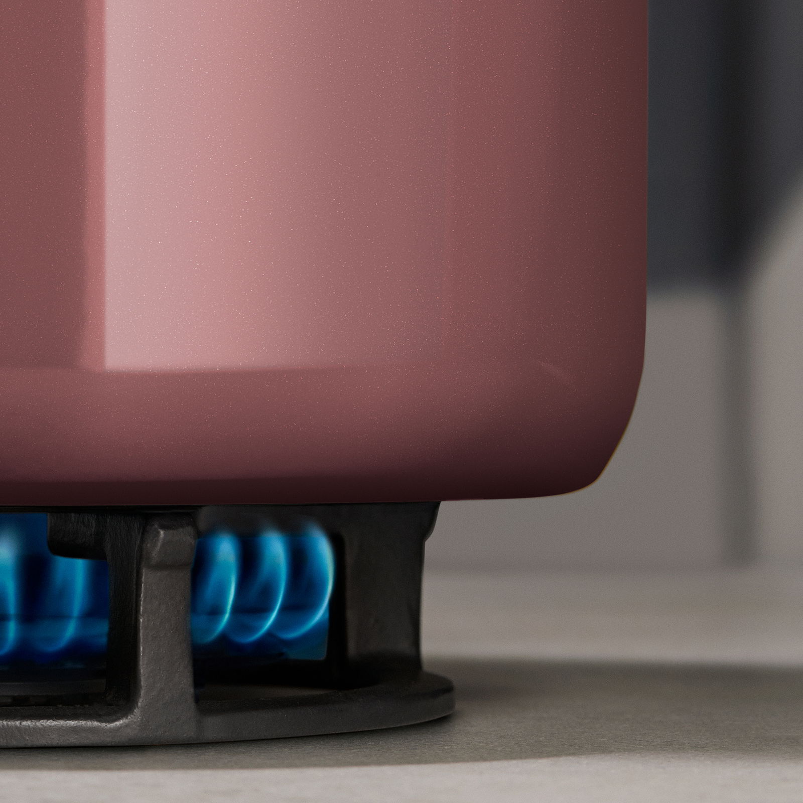 Nahaufnahme eines rosafarbenen Topfes auf einem Gasherd mit blauer Flamme.