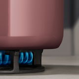 Nahaufnahme eines rosafarbenen Topfes auf einem Gasherd mit blauer Flamme.