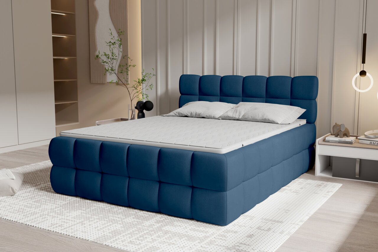 Modernes, gepolstertes Polsterbett in Dunkelblau mit quadratischer Steppung an Kopf- und Fußteil, weißer Matratze und zwei Kissen im Schlafzimmer; Perspektive: schräg von vorne links.