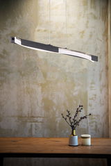 Moderne Pendelleuchte Bridge in seitlicher Perspektive über einem Holztisch mit Dekoration.