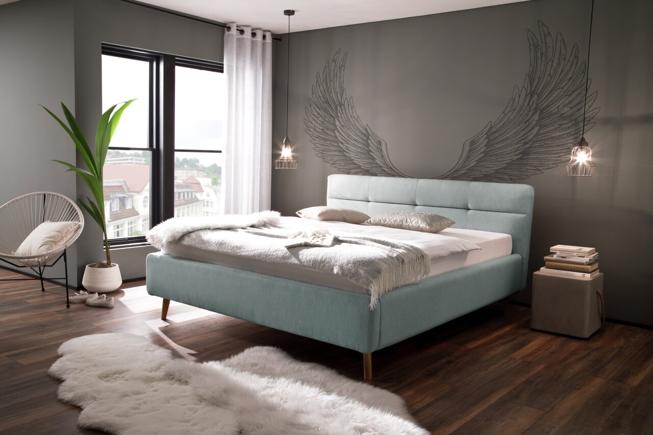 Modernes Polsterbett in einem stilvollen Schlafzimmer mit großen Fenstern, dekorativen Flügeln an der Wand und gemütlicher Atmosphäre, seitliche Perspektive.