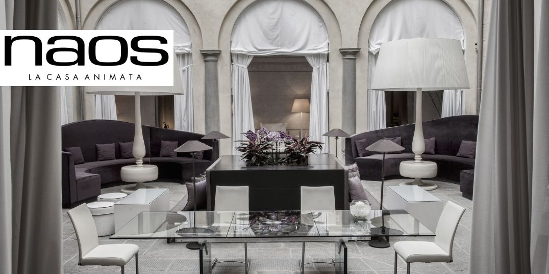 Anspruchsvolles Ambiente zeigt eine dunkle Indoor-Lounge und einen Glastisch mit weißen Stühlen. Logo Naos- La Casa Animata