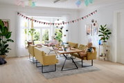 Gezellige eetkamer met gele banken en een houten tafel, versierd voor een feestje met ballonnen en slingers. Aanzicht vanaf de zijkant.