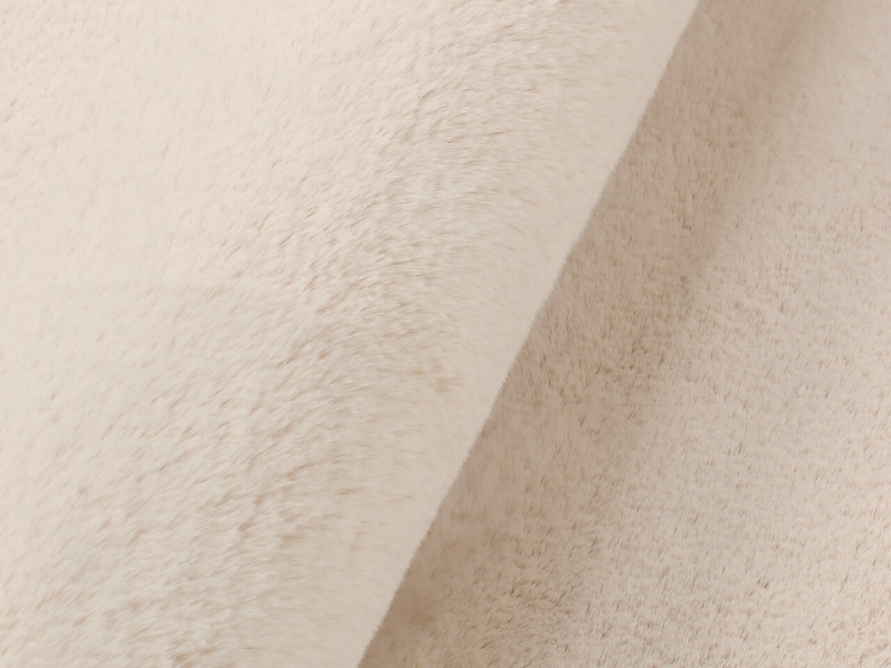 Nahaufnahme eines cremefarbenen Fellteppichs mit weicher Textur, seitliche Perspektive