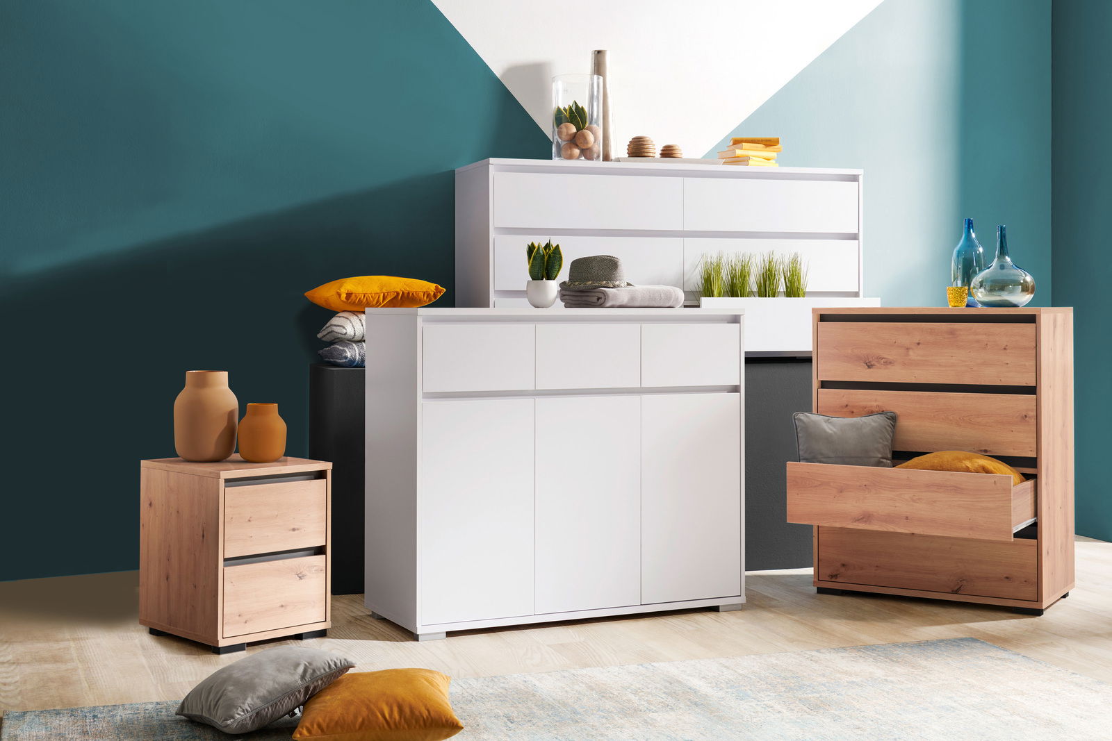 Carryhome Nachtkastje LINE Moderne Kommoden in verschiedenen Größen und Farben, frontal fotografiert. Eine weiße Kommode mit Schubladen und Türen, daneben eine Holzkommode mit offenen Schubladen. Dekorative Elemente wie Vasen und Kissen sind auf und um die Möbel platziert.