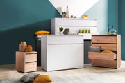 Moderne Kommoden in verschiedenen Größen und Farben, frontal fotografiert. Eine weiße Kommode mit Schubladen und Türen, daneben eine Holzkommode mit offenen Schubladen. Dekorative Elemente wie Vasen und Kissen sind auf und um die Möbel platziert.