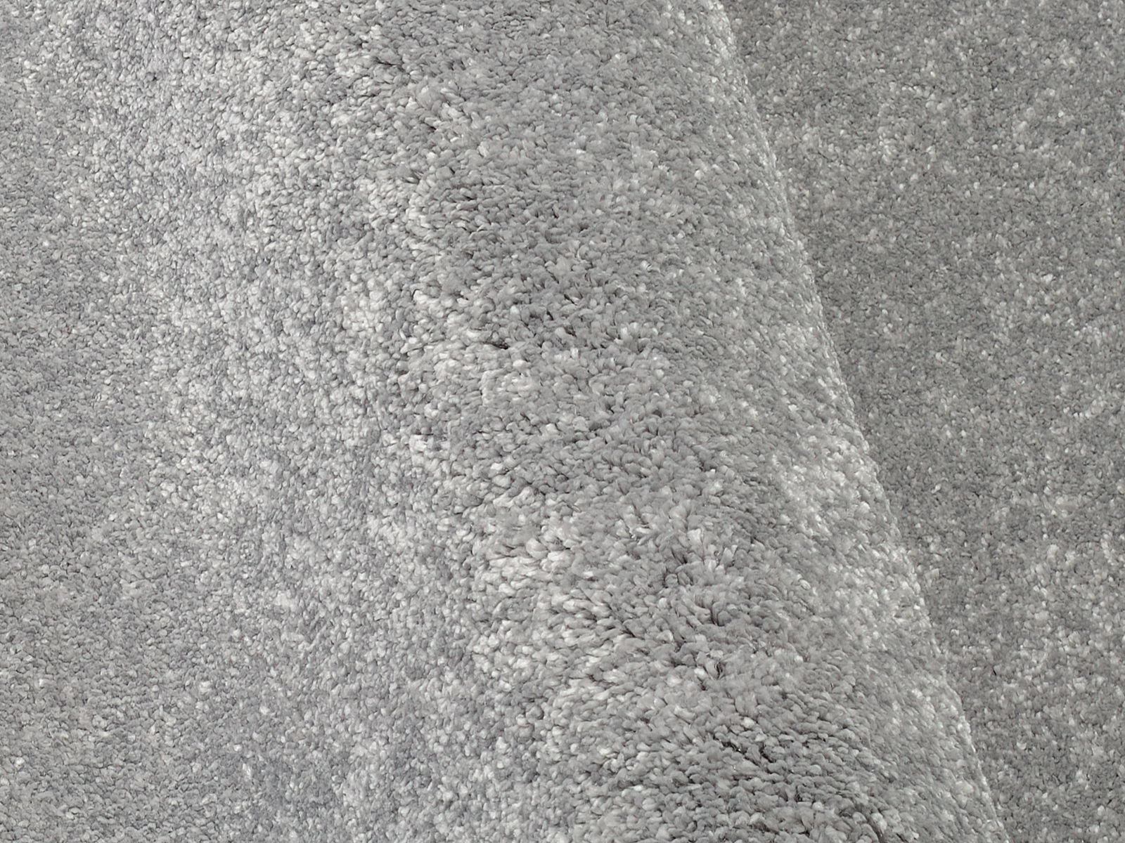Nahaufnahme eines grauen Uni-Teppichs mit weicher, flauschiger Textur, perspektivisch von der Seite aufgenommen.