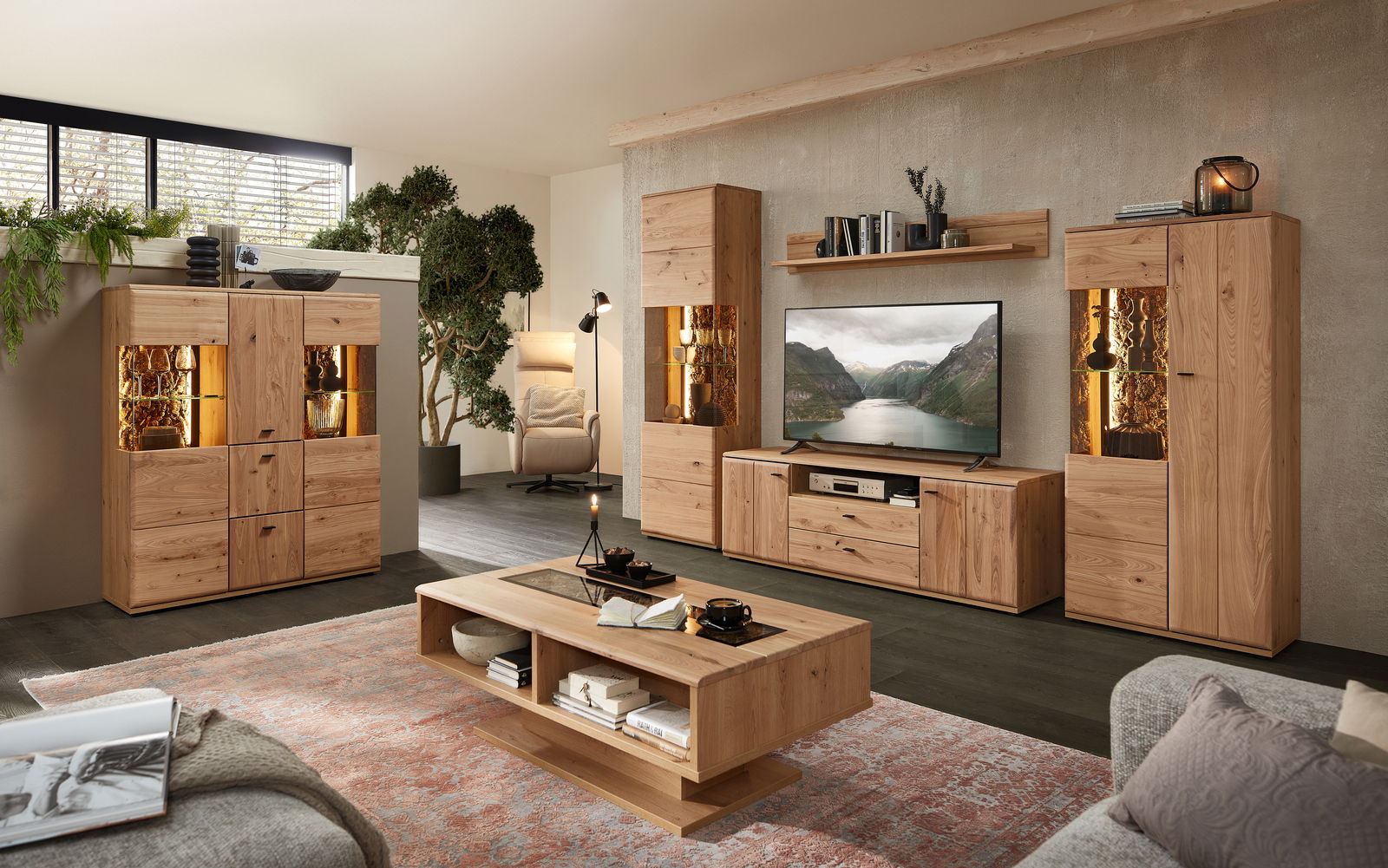 Wohnzimmer mit moderner Wandkombination aus Holz, bestehend aus Highboard, Sideboard und Wandregal, mit LED-Beleuchtung und dekorativen Elementen, Perspektive von vorne.