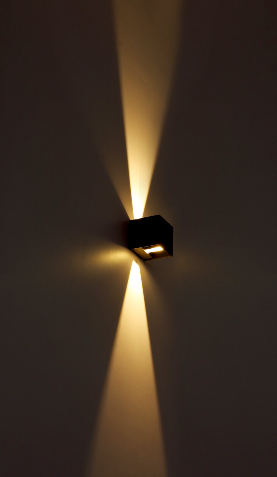 Moderne Außenleuchte in Würfelform, die warmes Licht nach oben und unten an die Wand strahlt, seitliche Perspektive.