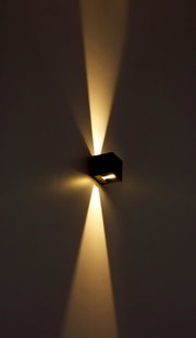 Moderne Außenleuchte in Würfelform, die warmes Licht nach oben und unten an die Wand strahlt, seitliche Perspektive.