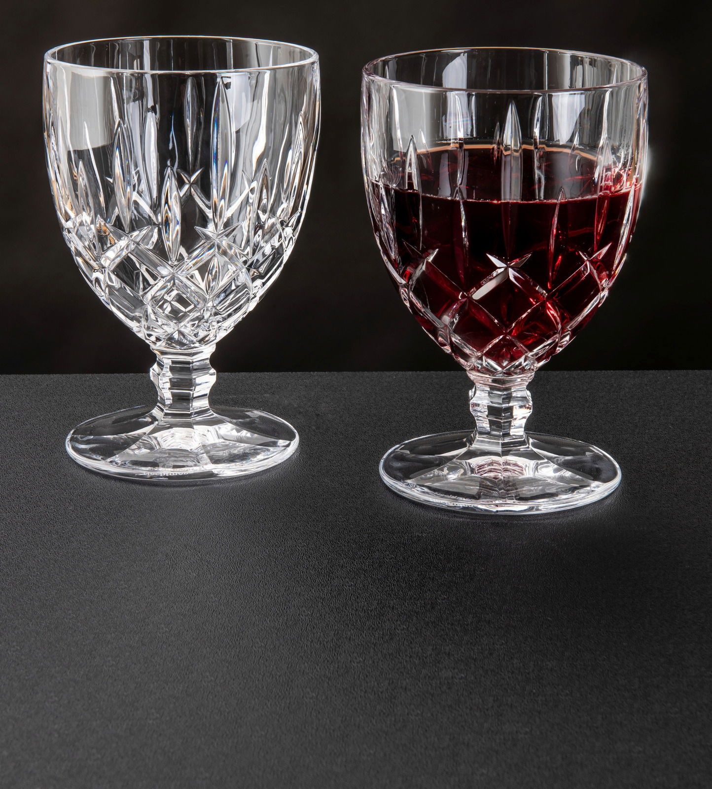 Zwei Weinkelche Noblesse 350ml aus Kristallglas, einer leer und einer mit Rotwein gefüllt, auf schwarzem Untergrund, seitliche Perspektive.
