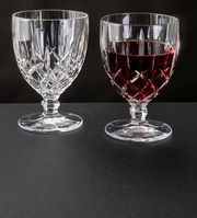 Zwei Weinkelche Noblesse 350ml aus Kristallglas, einer leer und einer mit Rotwein gefüllt, auf schwarzem Untergrund, seitliche Perspektive.