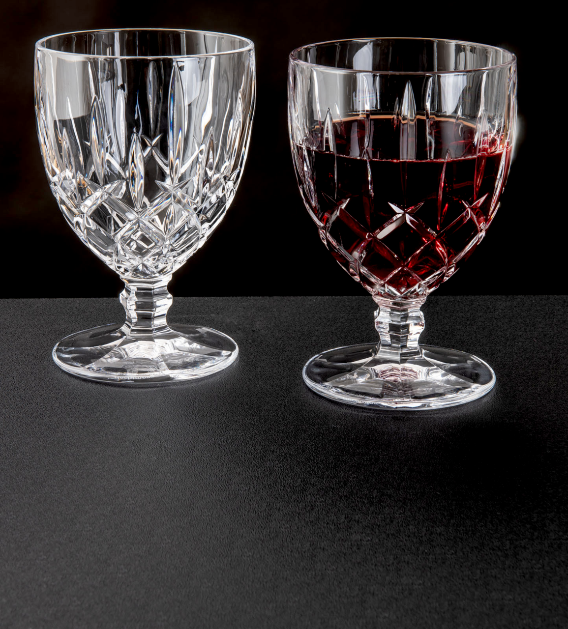 Zwei Weinkelche Noblesse 350ml aus Kristallglas, einer leer und einer mit Rotwein gefüllt, auf schwarzem Untergrund, seitliche Perspektive.