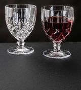 Zwei Weinkelche Noblesse 350ml aus Kristallglas, einer leer und einer mit Rotwein gefüllt, auf schwarzem Untergrund, seitliche Perspektive.