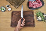 Fleischmesser 20cm VIER STERNE, gehalten in einer Hand über einem Schneidebrett, mit frischen Kräutern und Fleisch im Hintergrund, aus der Vogelperspektive.