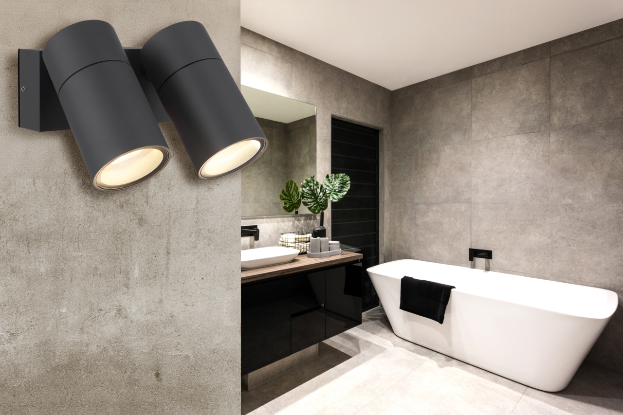 Moderne schwarze Außenwandleuchte mit zwei zylindrischen Strahlern, montiert an einer Betonwand in einem stilvollen Badezimmer. Perspektive von der Seite.