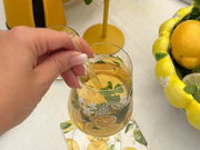 Hand rührt Zitronendrink im verzierten Weinglas auf sommerlich gedecktem Tisch.