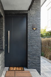 Moderne LED-Außenwandleuchte an einer Steinwand neben einer Haustür, seitliche Perspektive.