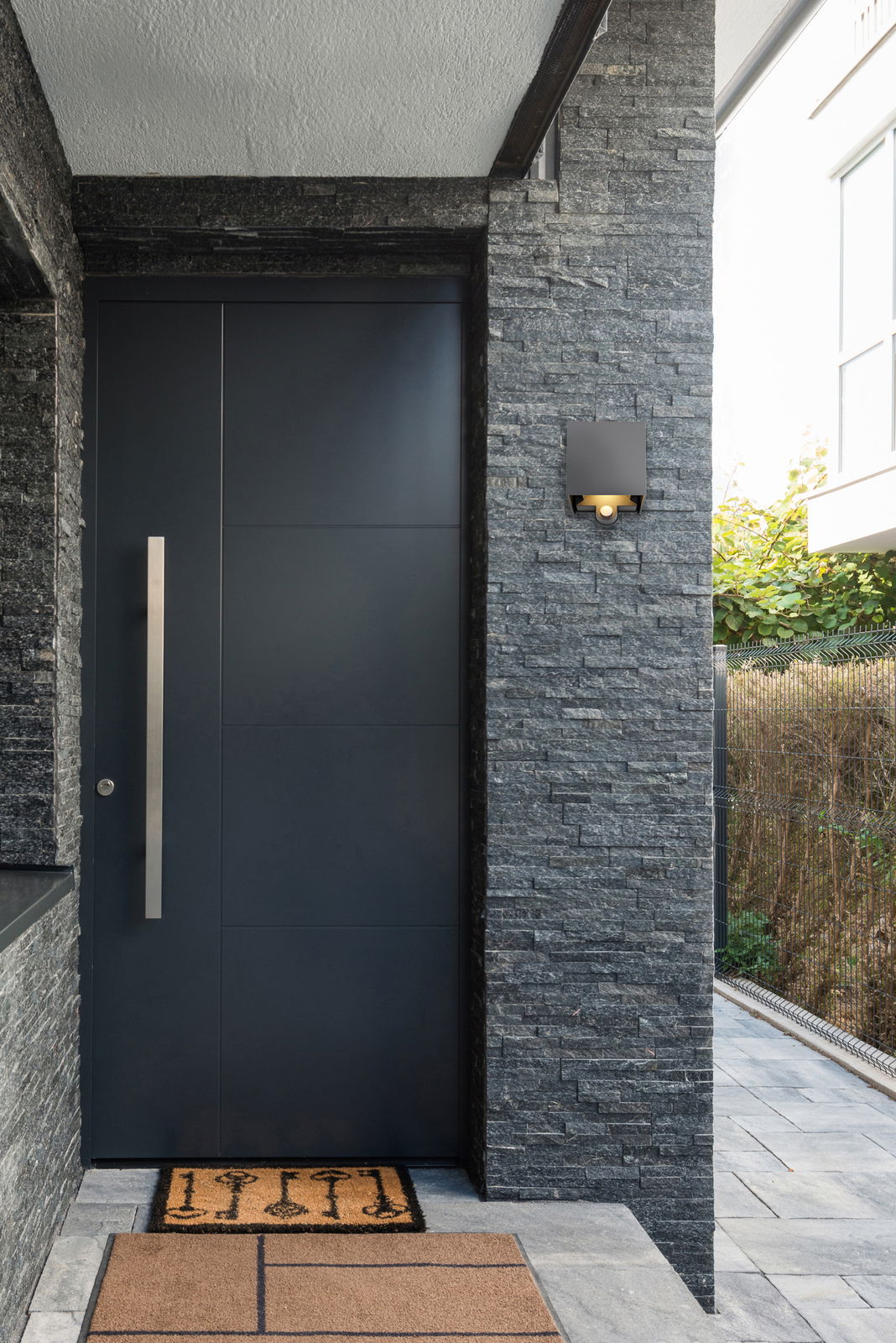 Moderne LED-Außenwandleuchte an einer Steinwand neben einer Haustür, seitliche Perspektive.