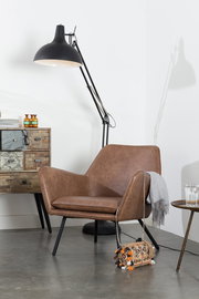Moderner brauner Ledersessel mit schwarzen Beinen, seitliche Perspektive, neben einer Stehlampe und einem Beistelltisch.