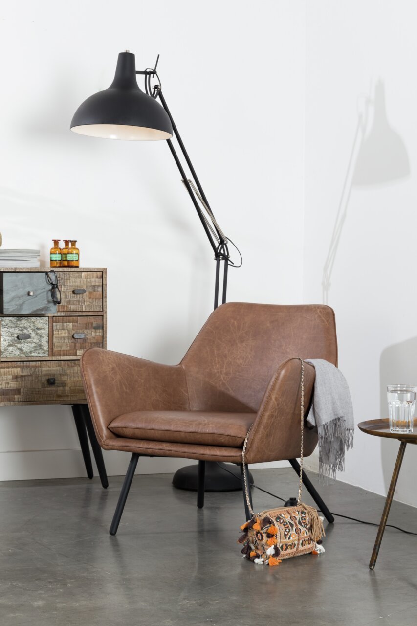 Moderner brauner Ledersessel mit schwarzen Beinen, seitliche Perspektive, neben einer Stehlampe und einem Beistelltisch.