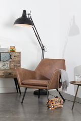Moderner brauner Ledersessel mit schwarzen Beinen, seitliche Perspektive, neben einer Stehlampe und einem Beistelltisch.