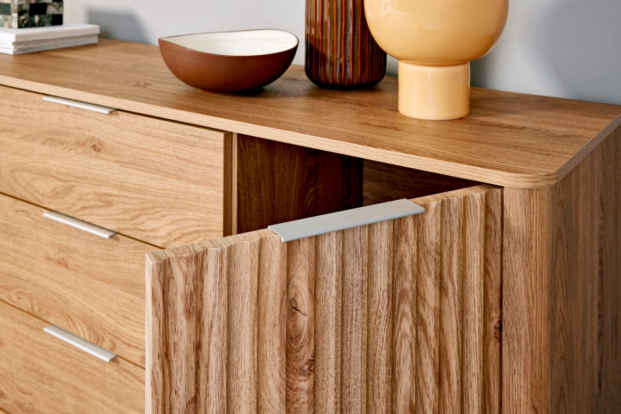 Nahaufnahme eines modernen Sideboards aus Holz mit geöffneter Tür, dekoriert mit Schalen und Vasen, aus seitlicher Perspektive.