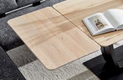 Esstisch aus hellem Holz mit abgerundeten Ecken, von oben fotografiert, mit einem aufgeschlagenen Buch auf der Tischplatte.