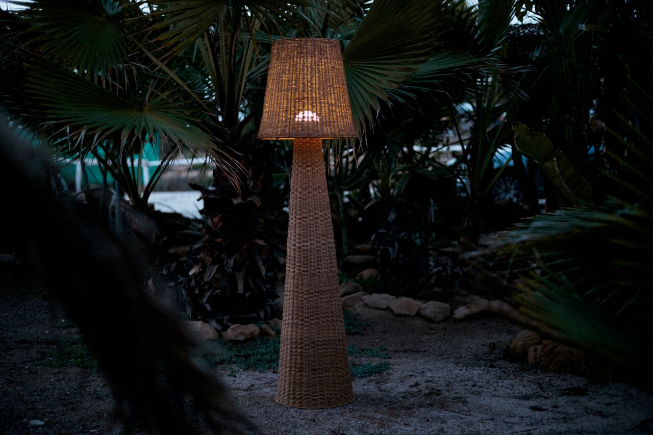 Akku-Outdoor-Stehleuchte aus Rattan in einem Garten bei Dämmerung, seitliche Perspektive